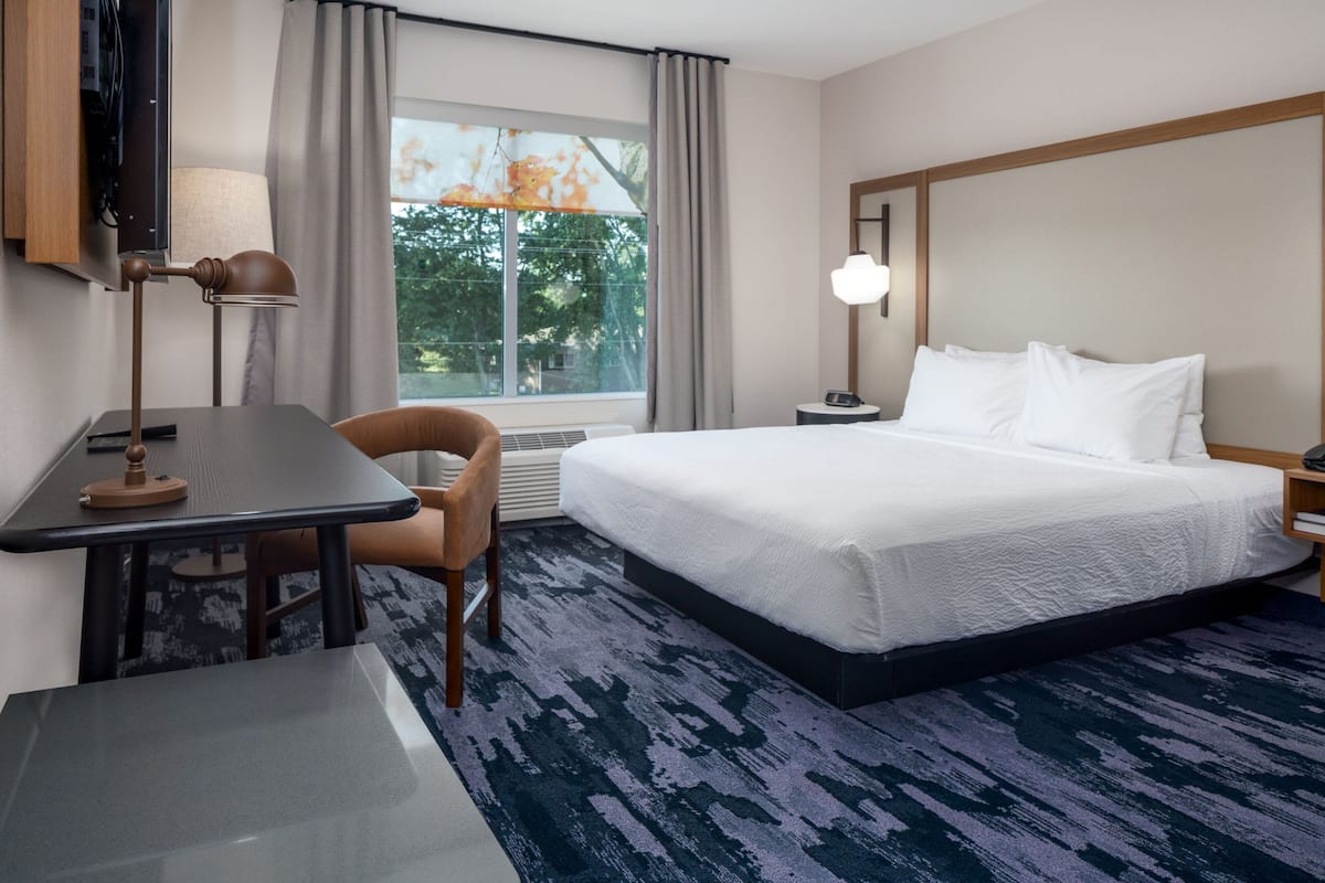 Ein Hotelzimmer mit Bett, Schreibtisch, Stuhl, Fernseher und einem Fenster mit Vorhängen.