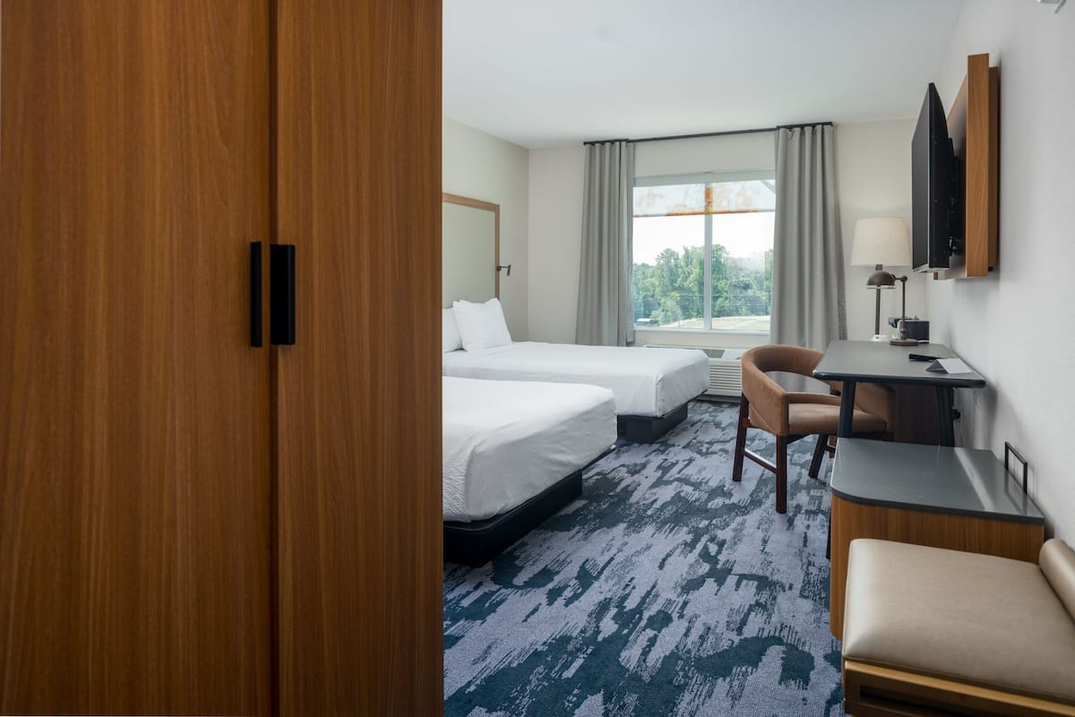 Ein Hotelzimmer mit zwei Betten, einem Schreibtisch, einem Stuhl, einem Fernseher und einem Fenster mit Vorhängen.