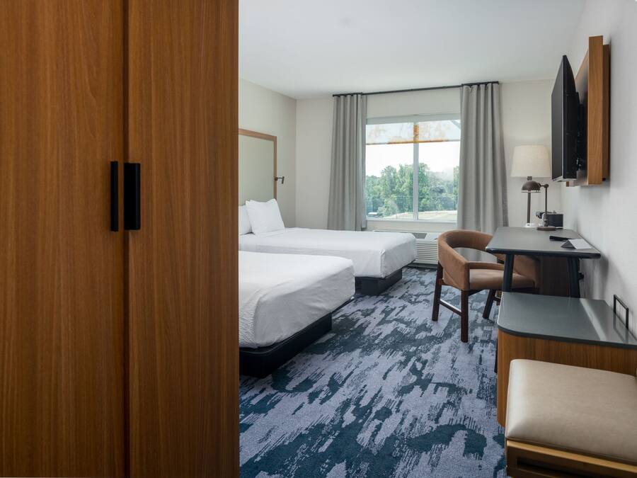 A hotel room with two beds, a desk, a chair, a TV, and a window with curtains.