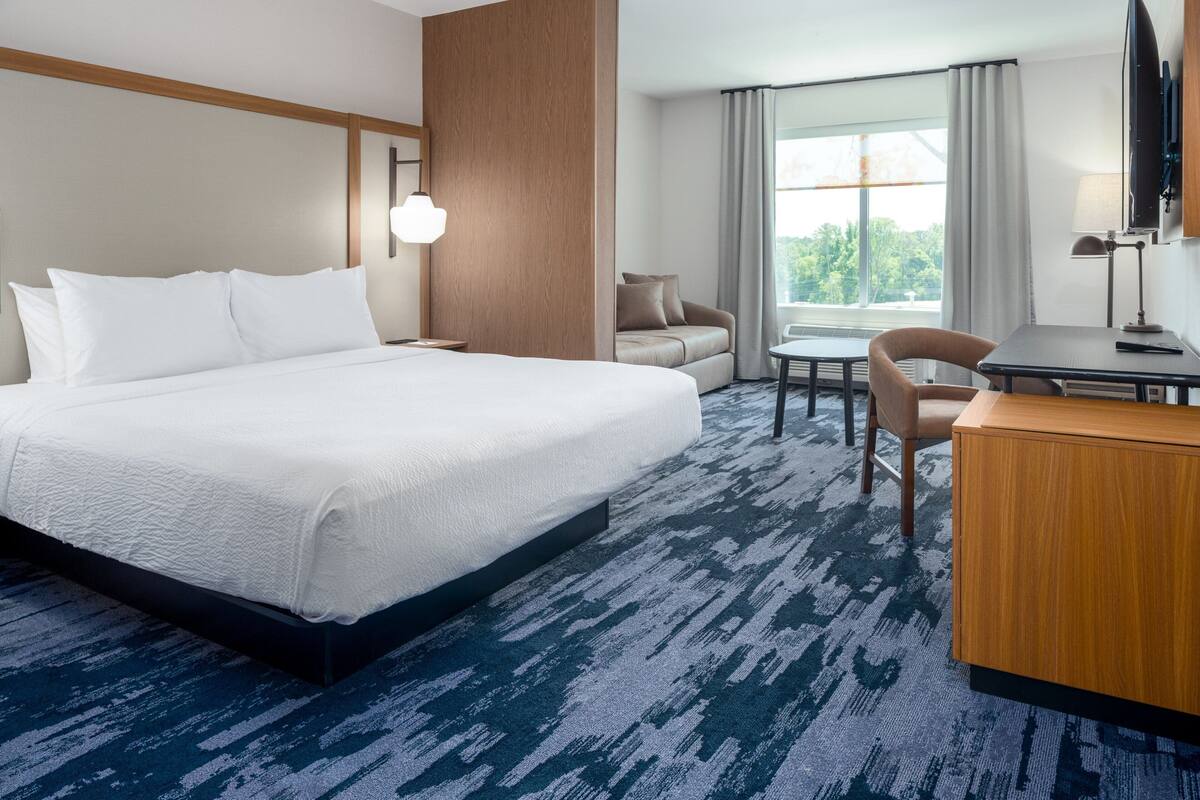 Ein Hotelzimmer mit einem großen Bett, einem Schreibtisch, einem Sessel, einer Couch und einem Vorhangfenster.