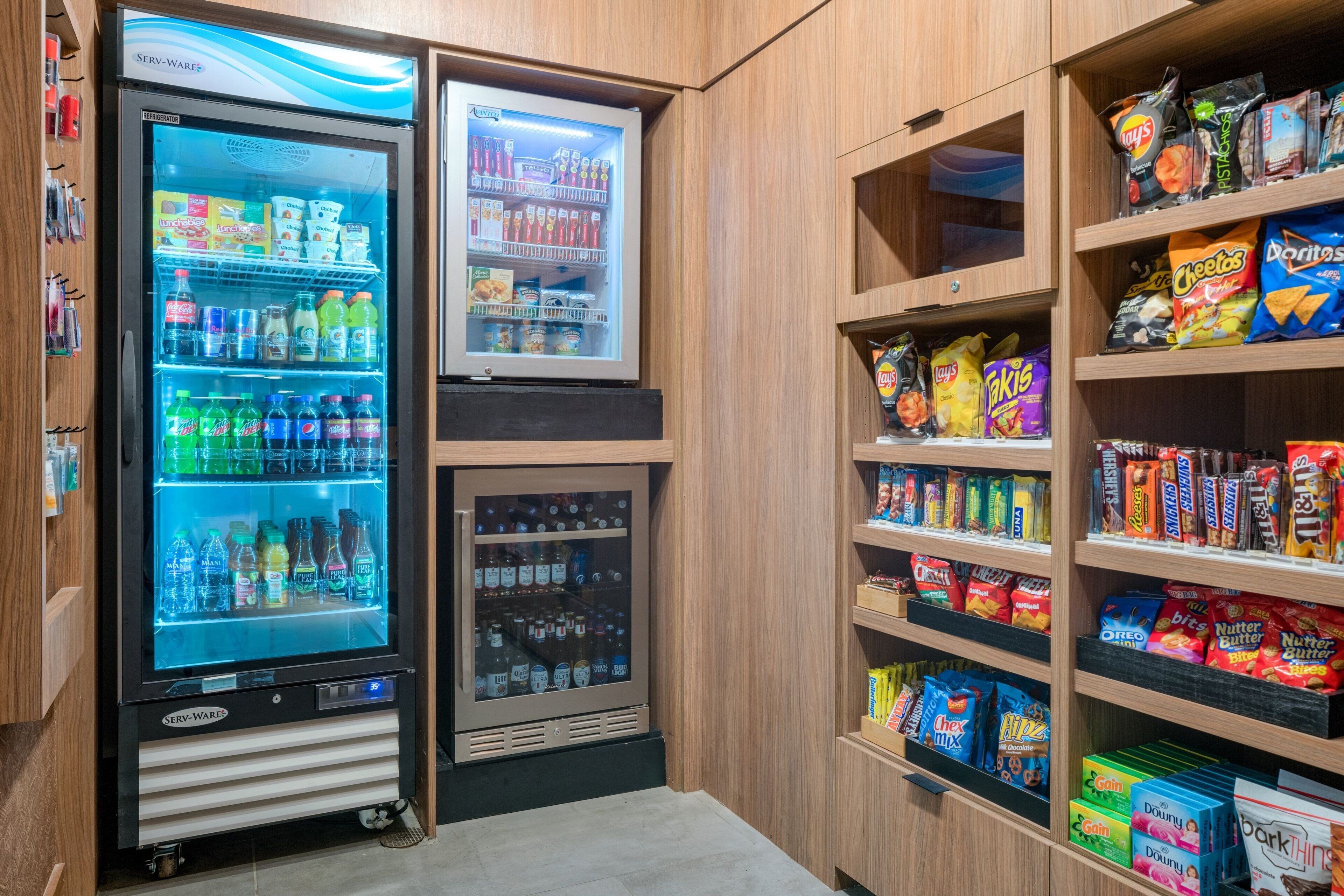A vending machine with various drinks and snacks, surrounded by wooden shelves stocked with snacks and packaged goods.
