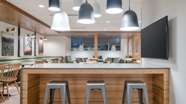 Een modern restaurant met een centraal eiland, barstoelen, hanglampen en een grote flatscreen televisie.