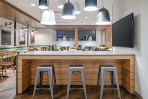 Un restaurante moderno con una isla central, taburetes de bar, iluminación colgante y un televisor de pantalla plana grande.