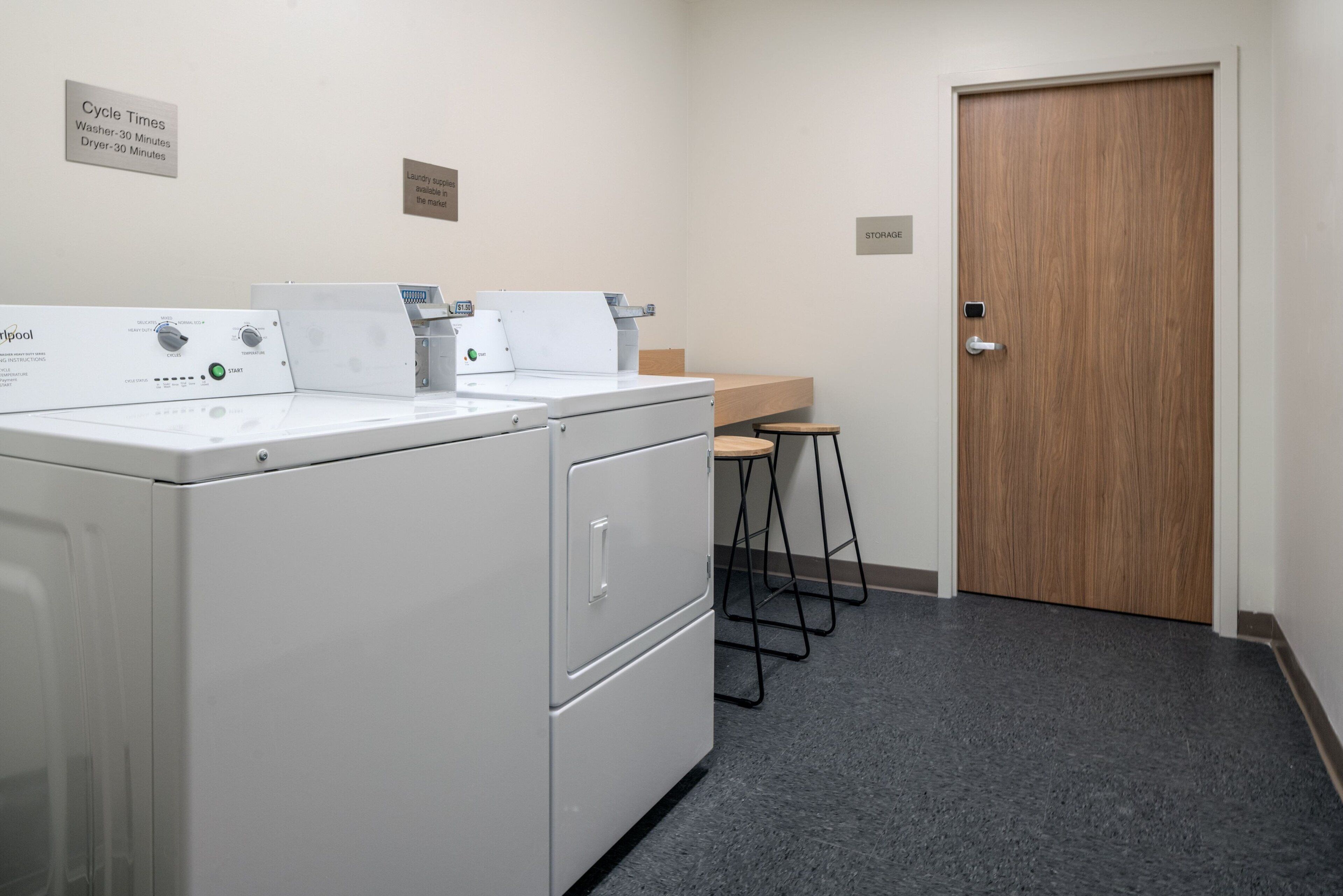 A laundry area with a front-loading washer and dryer, a wooden counter, and a door labeled "STORAGE".