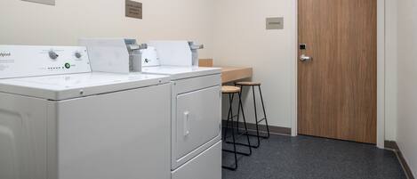 Un espace buanderie équipé d’un lave-linge et d’un sèche-linge à chargement frontal, d’un plan de travail en bois et d’une porte portant l’inscription « RANGEMENT ».