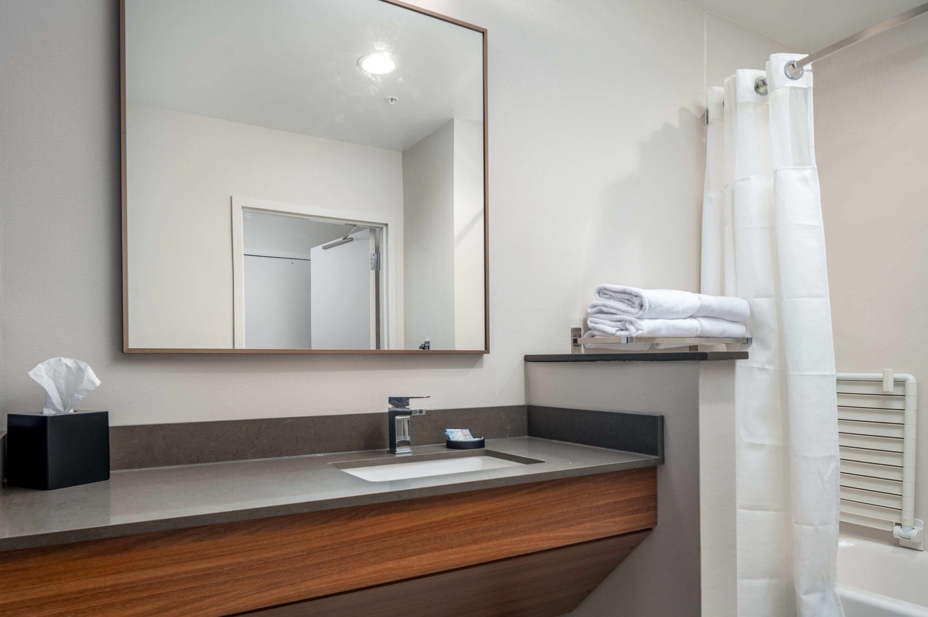 A bathroom with a wooden vanity, a sink, a mirror, a towel rack, and a shower curtain.