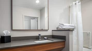 A bathroom with a wooden vanity, a sink, a mirror, a towel rack, and a shower curtain.