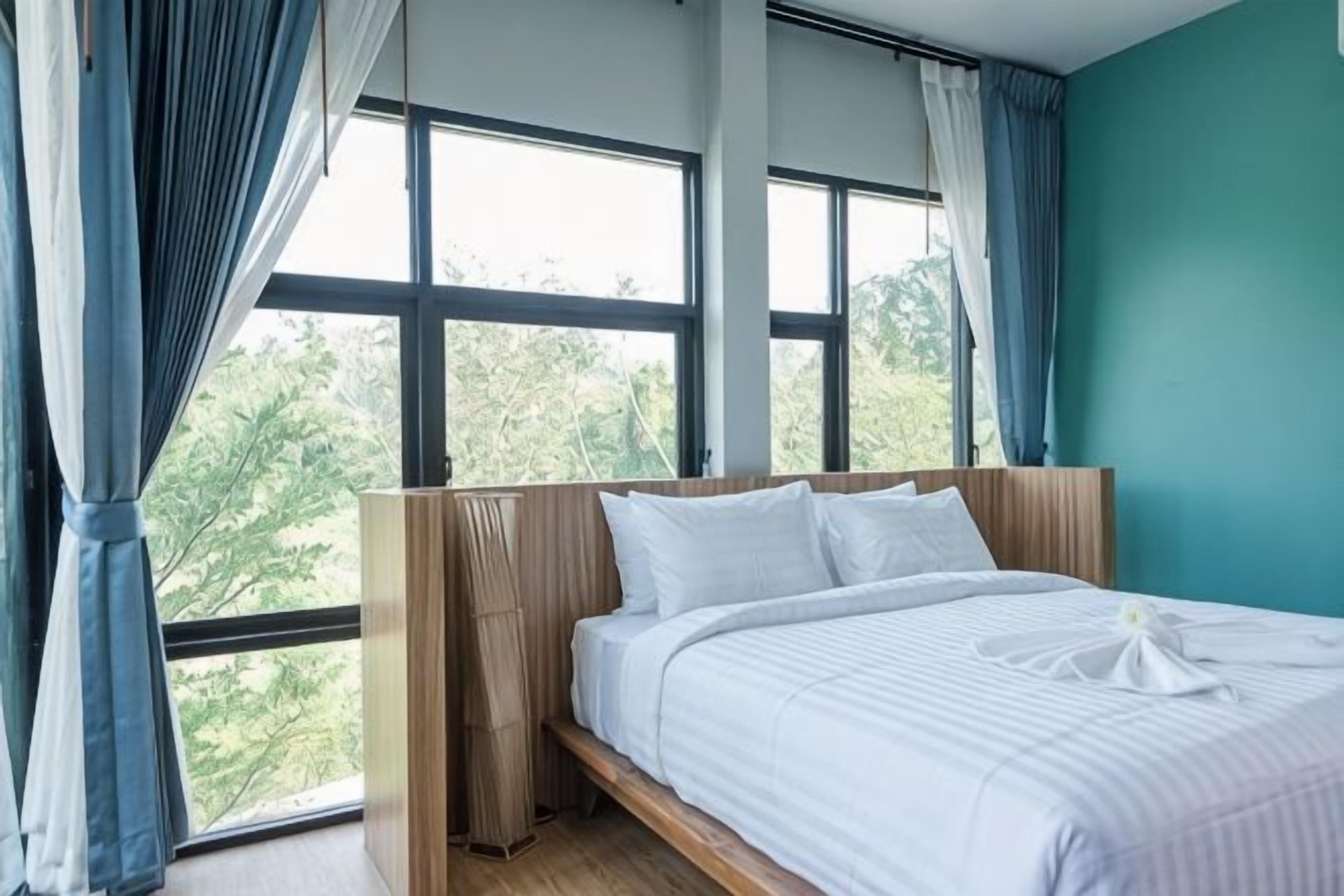 A bedroom with a bed, large windows, and a view of greenery.