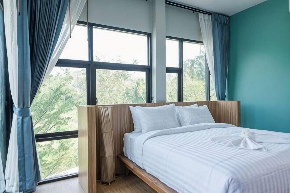 Un dormitorio con cama, ventanas amplias y vistas a zonas verdes.