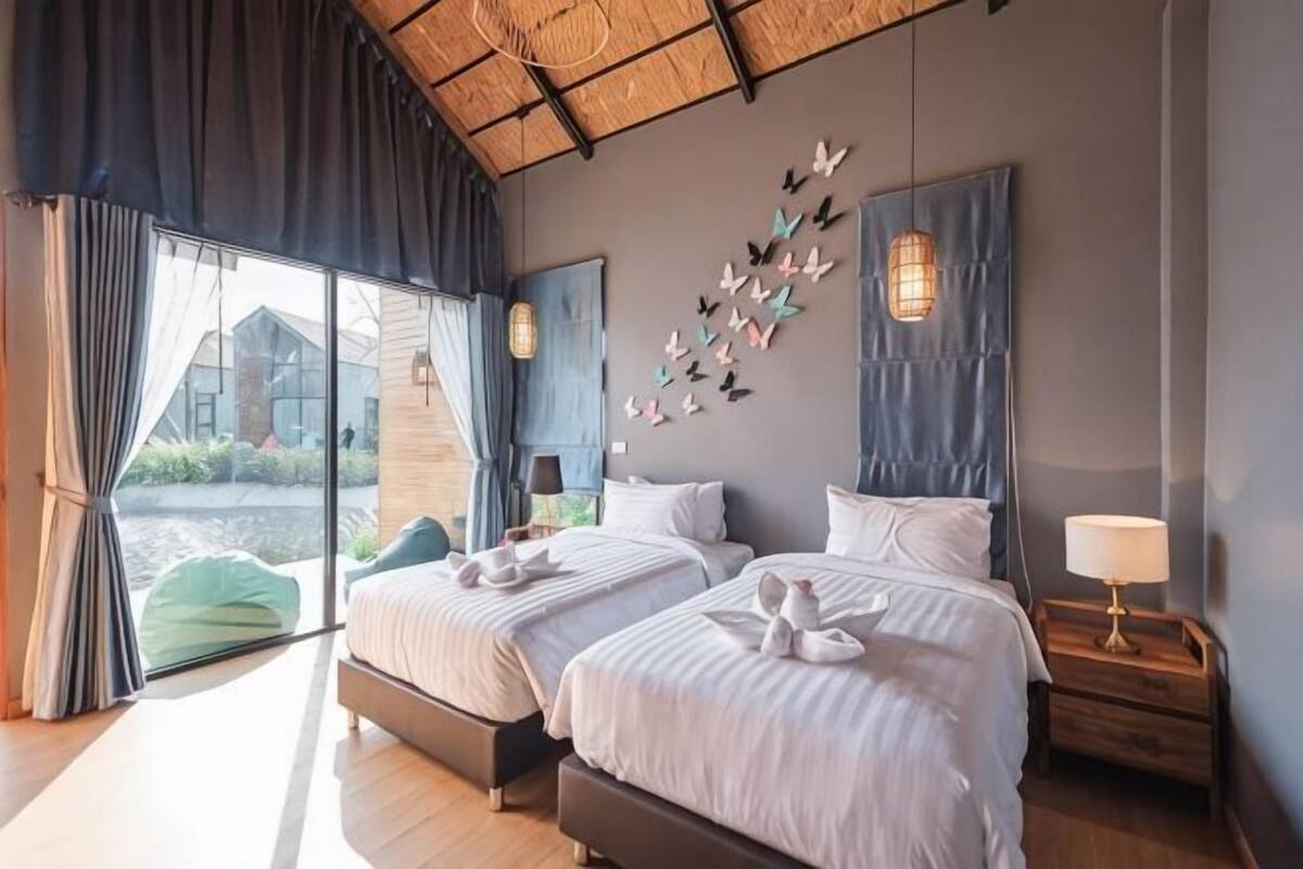 A bedroom with two beds, a large window, and a view of a building outside.