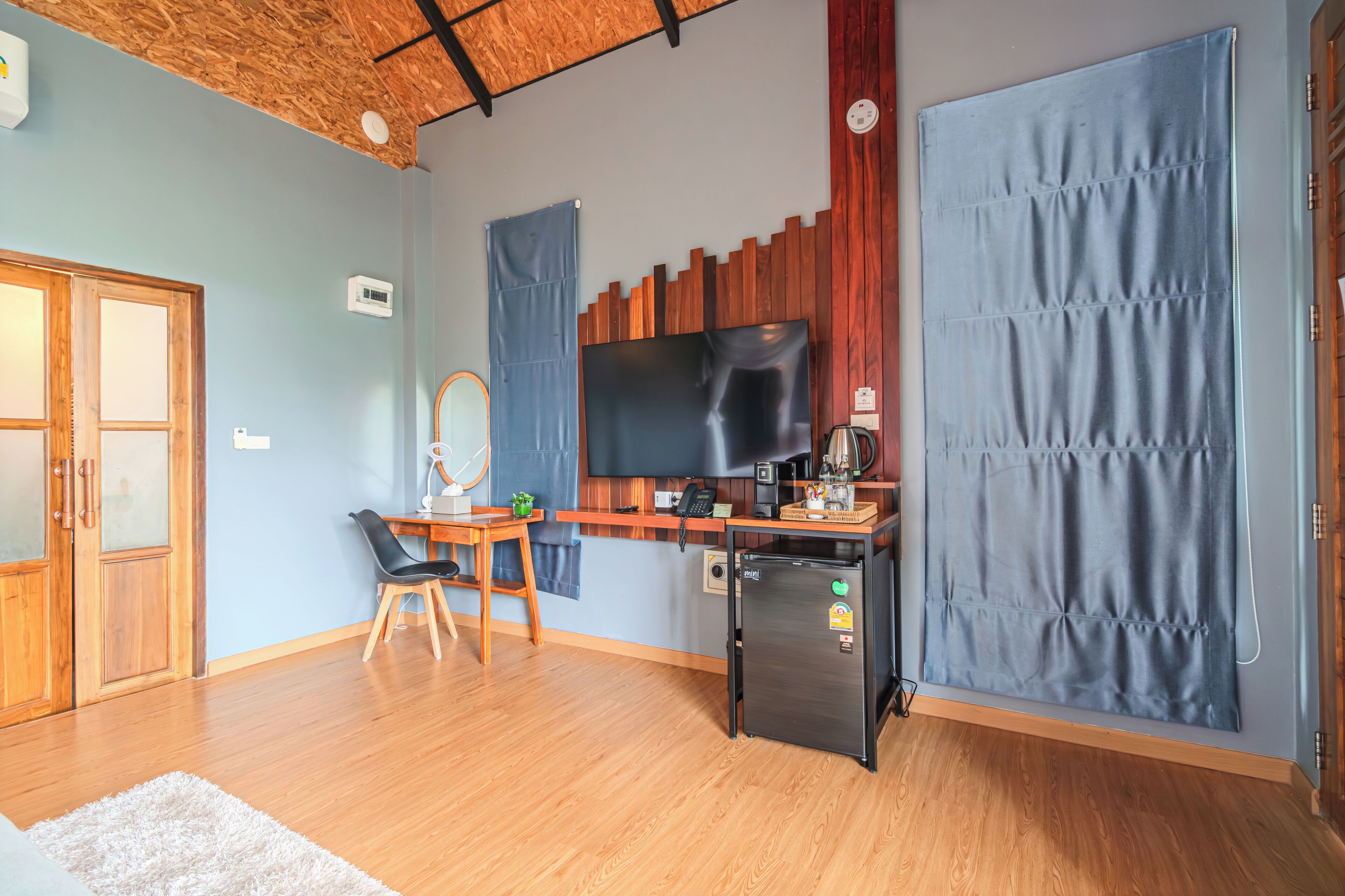 A compact kitchen with wooden cabinets, a built-in TV, a refrigerator, and a dining area with a chair and table.