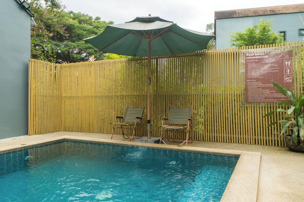 Piscina con dos sillas de descanso y una sombrilla, rodeada por una cerca de bambú.