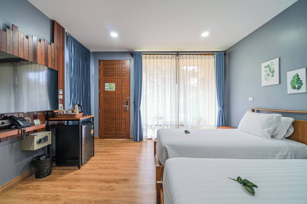 Habitación de hotel con dos camas, un escritorio con teléfono y radio, un refrigerador pequeño y un armario de madera.