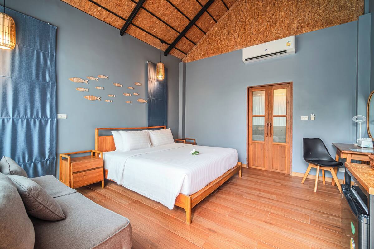 Un dormitorio con una cama de madera, una mesita de noche de madera, un escritorio de madera, una silla, un sofá y una pared decorada con motivos de peces.