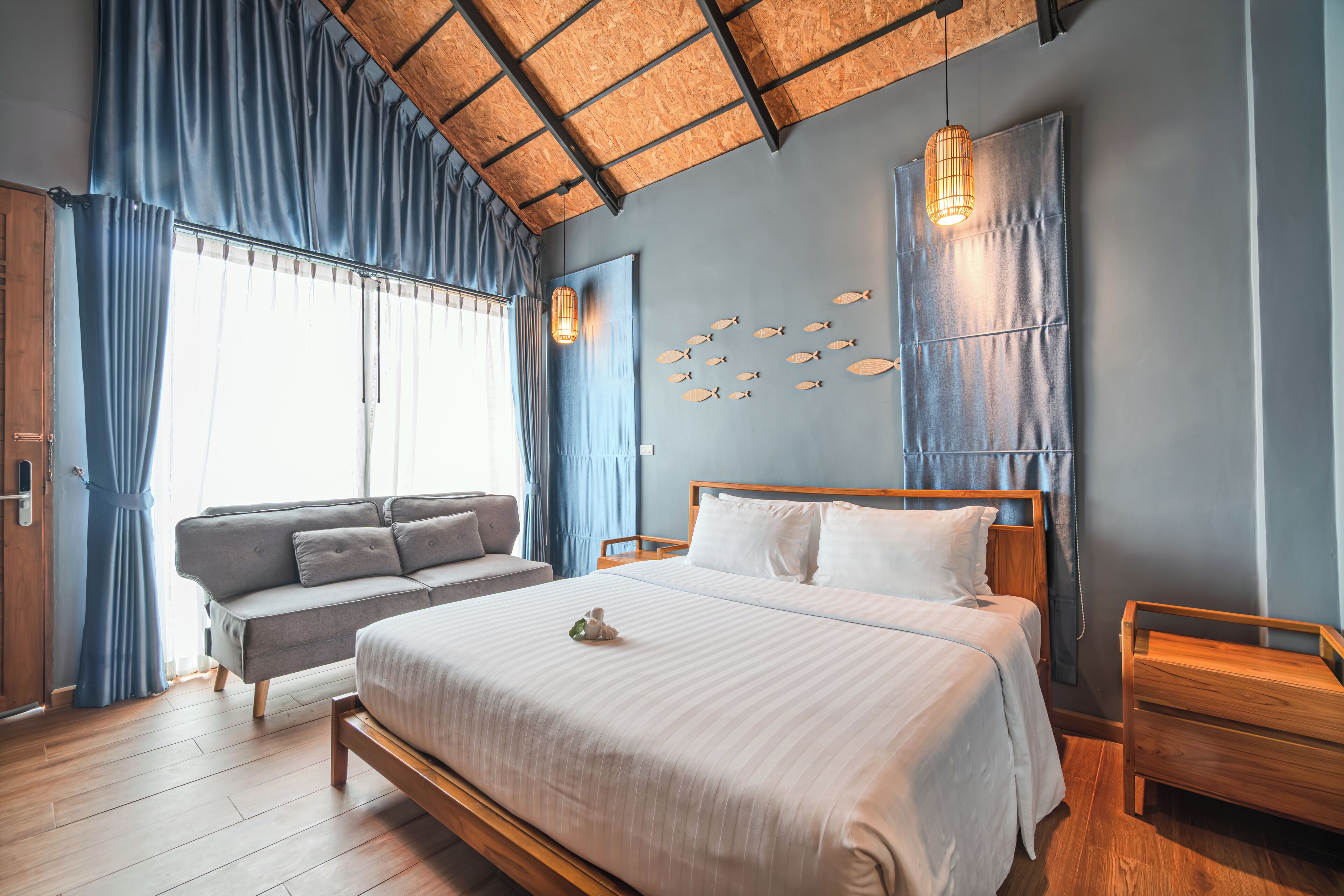 A bedroom with a large bed, a sofa, a wooden nightstand, and a wall-mounted fish decoration.