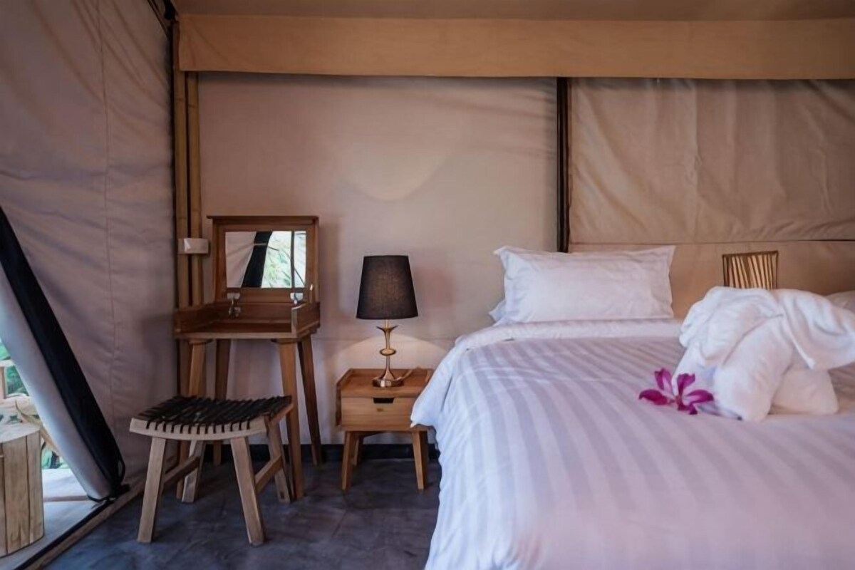 Una habitació tipus tenda amb un llit, una taula petita amb una làmpada i una cadira.