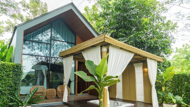 A modern house with a large glass window, a wooden deck, and a garden with potted plants. - The Tree Riverside Resort Kaeng Krachan (Kaeng Krachan)