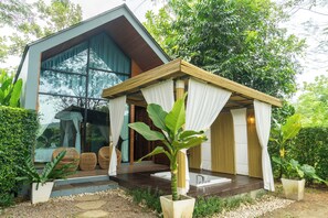 A modern house with a large glass window, a wooden deck, and a garden with potted plants. - The Tree Riverside Resort Kaeng Krachan (Kaeng Krachan)