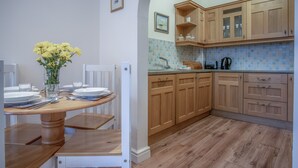 Cozinha com armários de madeira, painel de azulejos e uma área de jantar com mesa e cadeiras de madeira.