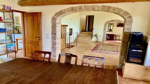 Zona pranzo con tavolo e sedie in legno, un arco che conduce a una scala e una cucina visibile sullo sfondo.