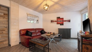 Un salon moderne avec un canapé en cuir rouge, une table basse en verre et un téléviseur posé sur un meuble en bois.