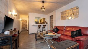 Un salon moderne avec un canapé en cuir rouge, une table basse en verre et un téléviseur posé sur un meuble en bois.