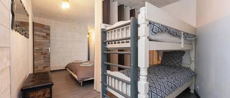 A bunk bed room with a wooden floor, a small bedside table, and a wall-mounted light fixture.