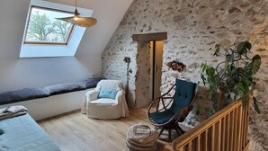 A loft-style room with a sloped ceiling, a stone wall, a wooden staircase, a bench, a chair, and a large window. - Cozy rental in Blomard with shared pool and pet-friendly (Blomard)