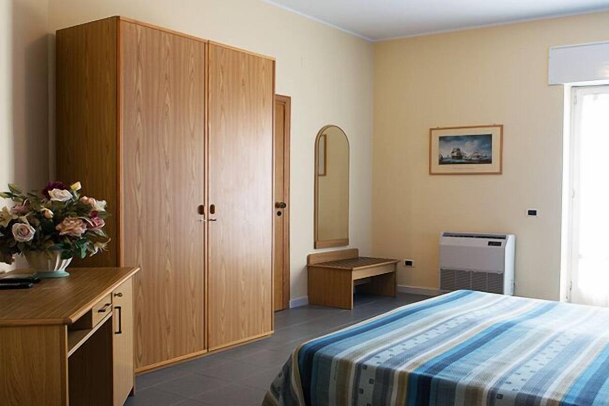 Ein Schlafzimmer mit Holzschrank, einem Bett mit gestreifter Bettwäsche, einer Bank, einem Spiegel und einem Heizkörper.