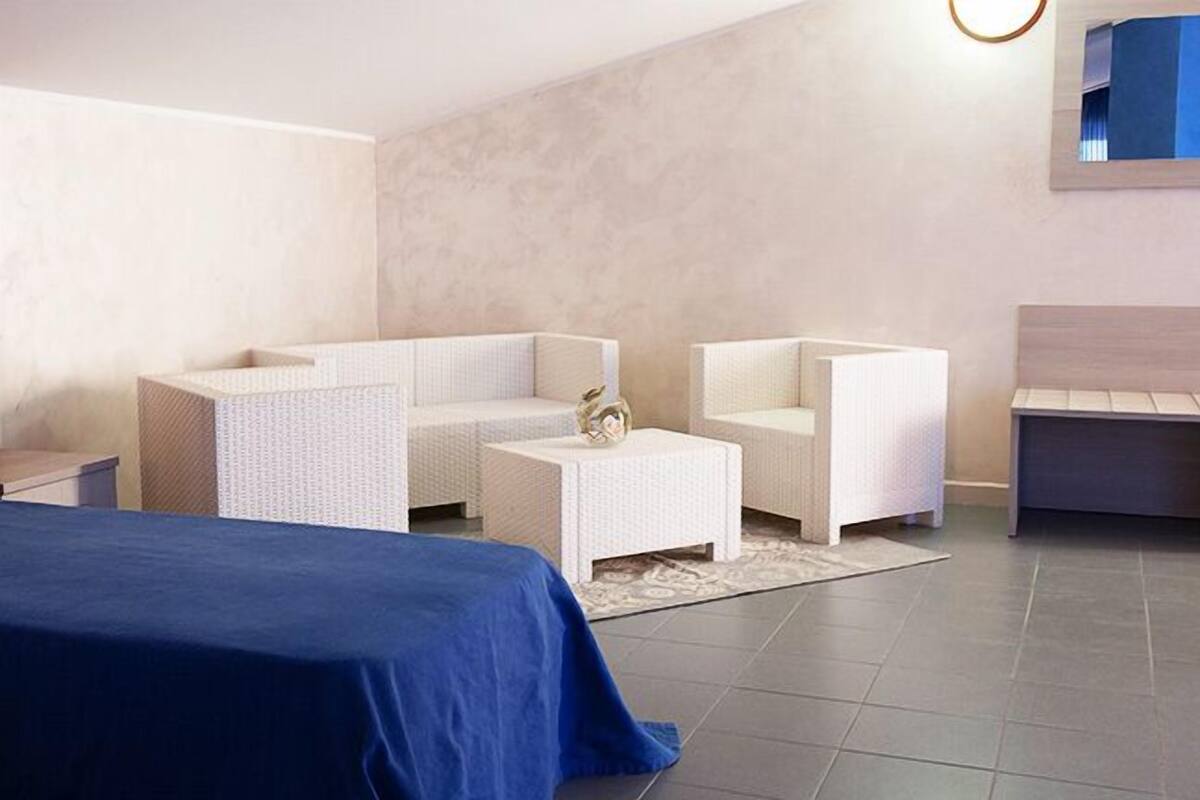 Ein modernes Hotelzimmer mit einem Bett, zwei weißen Sofas, einem kleinen Tisch und einem Nachttisch.