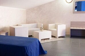 Una habitación de hotel moderna con una cama, dos sofás blancos, una mesita y una mesita de noche.