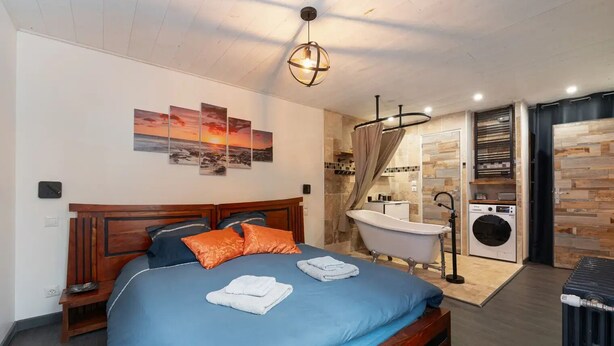 A bedroom with a wooden bed, a blue mattress, and a nightstand. There is a bathroom with a bathtub, a toilet, and a washing machine.