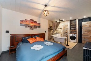 A bedroom with a wooden bed, a blue mattress, and a nightstand. There is a bathroom with a bathtub, a toilet, and a washing machine. - Gîte *** Gwenn Ha Du - Estate with SPA (Meslan)