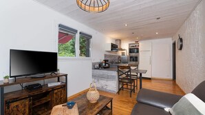 A modern living room with a TV, wooden furniture, a dining area, and a kitchen in the background.