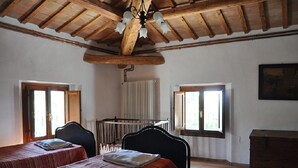 Une chambre avec deux lits, des poutres en bois au plafond, un radiateur et une fenêtre avec des rideaux.