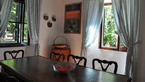 Une salle à manger avec une table en bois, quatre chaises, un saladier en verre rempli de fruits, un panier et un tableau encadré accroché au mur.