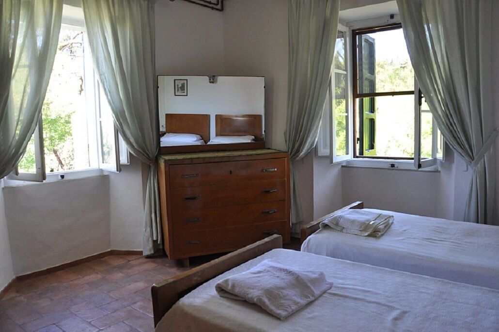 A bedroom with two beds, a wooden dresser, and a window with curtains.