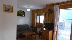 A living room with a sofa, a wooden dresser, a television, and a window with curtains. - 2-room cabin apartment, 6 ppl, parking in Les Contamines-Montjoie (Les Contamines-Montjoie)
