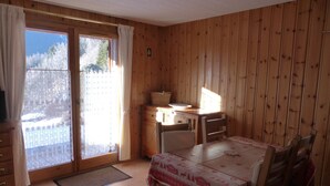 A wooden-paneled room with a dining table, chairs, a small kitchen area, and a sliding glass door leading to a balcony. - 2-room cabin apartment, 6 ppl, parking in Les Contamines-Montjoie (Les Contamines-Montjoie)