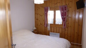 A bedroom with wooden paneling, a bed, a nightstand with a lamp, and a window with curtains. - 2-room cabin apartment, 6 ppl, parking in Les Contamines-Montjoie (Les Contamines-Montjoie)