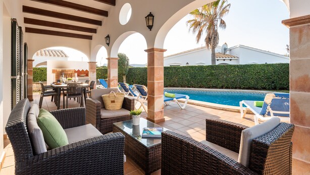 Een terras buiten met wicker meubels, een zwembad en een eethoek.