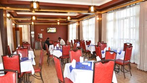 Un restaurant avec des chaises rouges et des nappes blanches, des poutres en bois au plafond et de grandes fenêtres avec des rideaux.