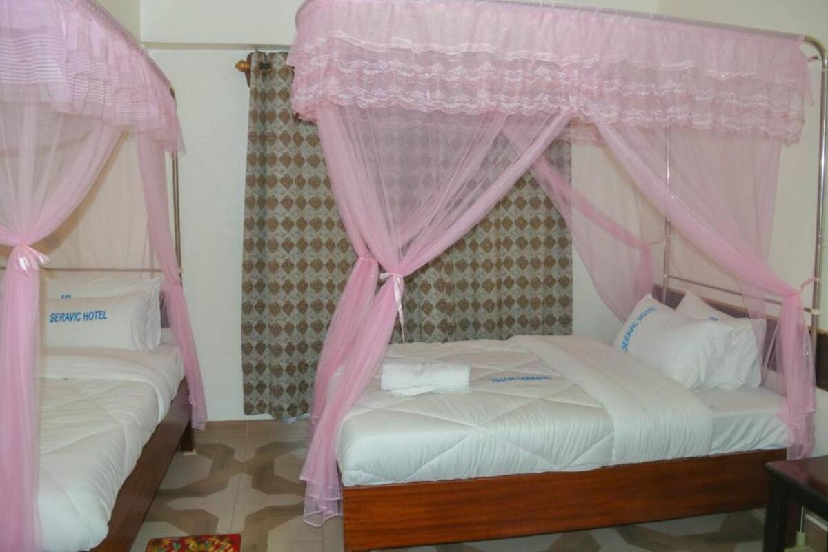Una habitación con dos camas, cada una con dosel y almohadas con la etiqueta "SERAVIC HOTEL".