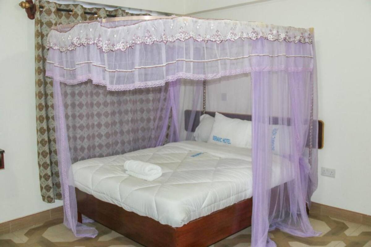 Una cama individual con dosel, una almohada con el texto "JERUSALEM HOTEL" y una cortina estampada.