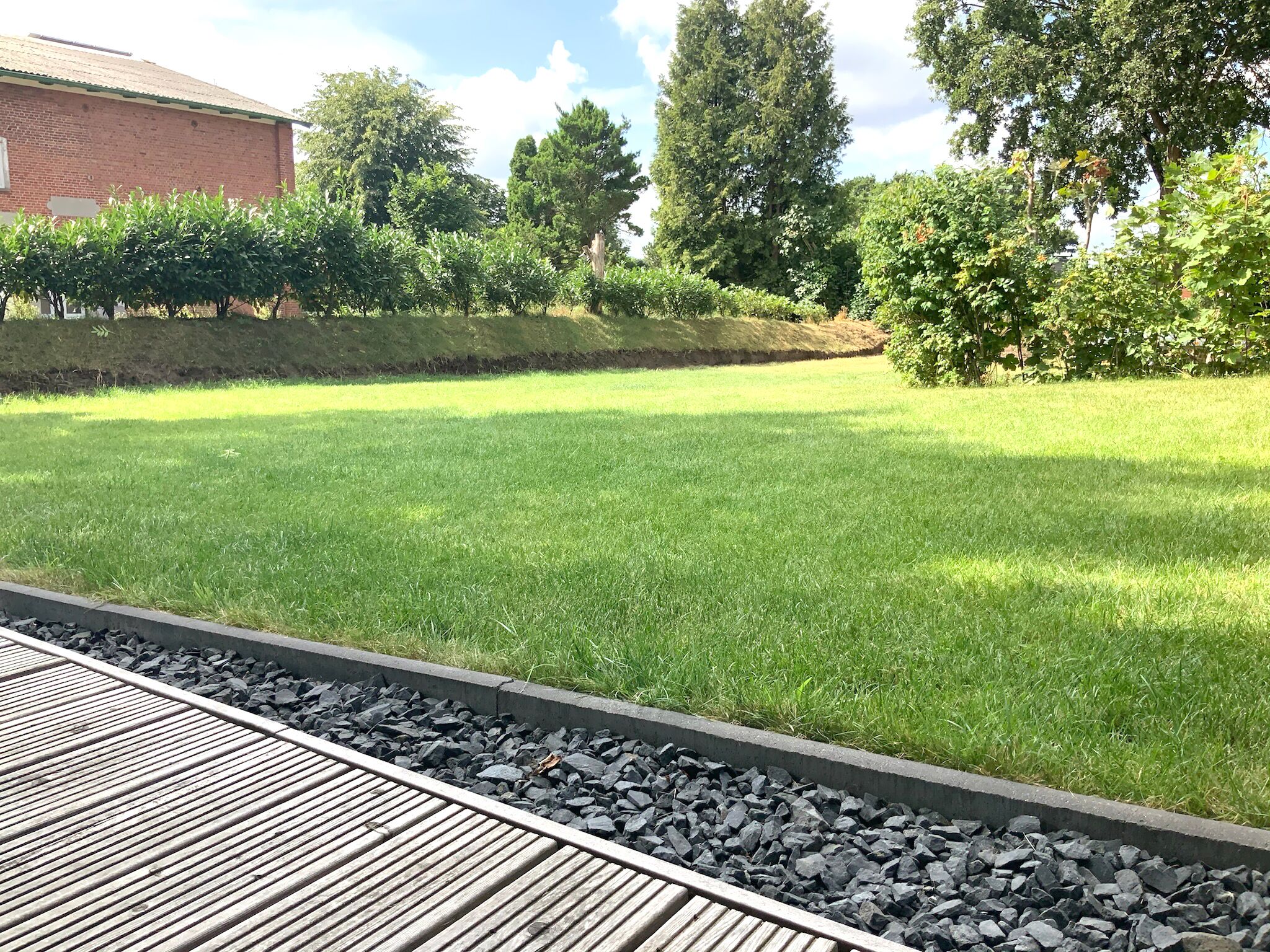 Une zone herbeuse avec une terrasse en bois et une bordure en pierre.