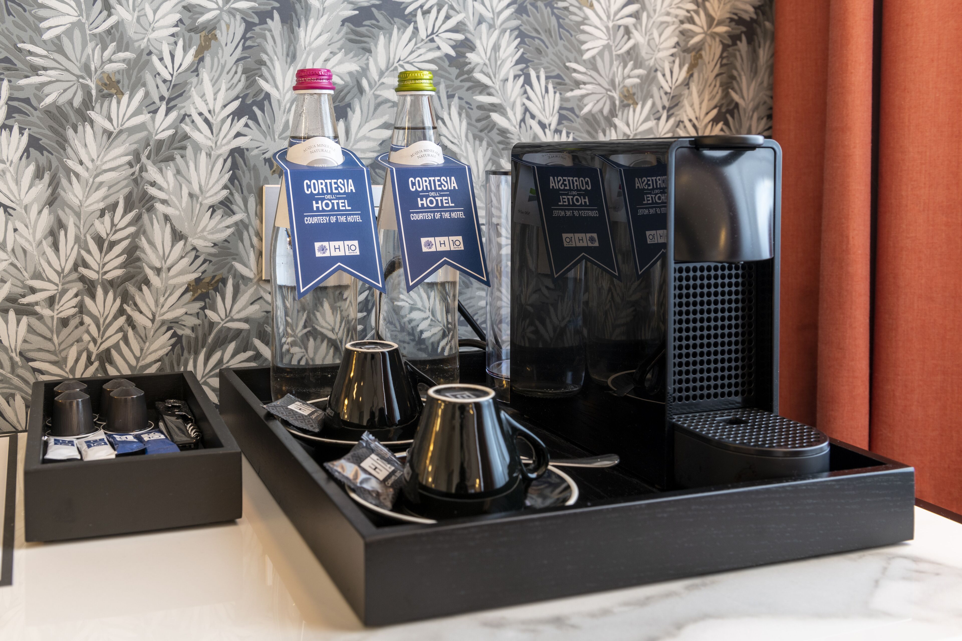 Un coin café comprenant deux bouteilles d’alcool de la marque Cortezia Hotel, une machine à café et divers accessoires pour préparer le café.