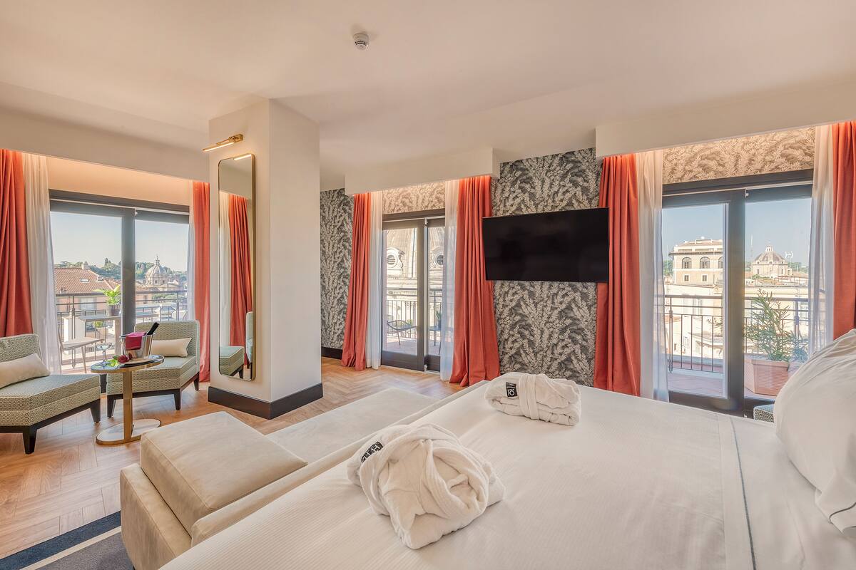 A hotel room with a bed, a sofa, a TV, and large windows with curtains.