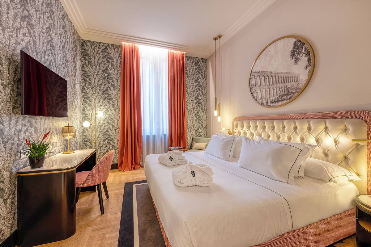 A hotel room with a large bed, a desk, a chair, and a television.