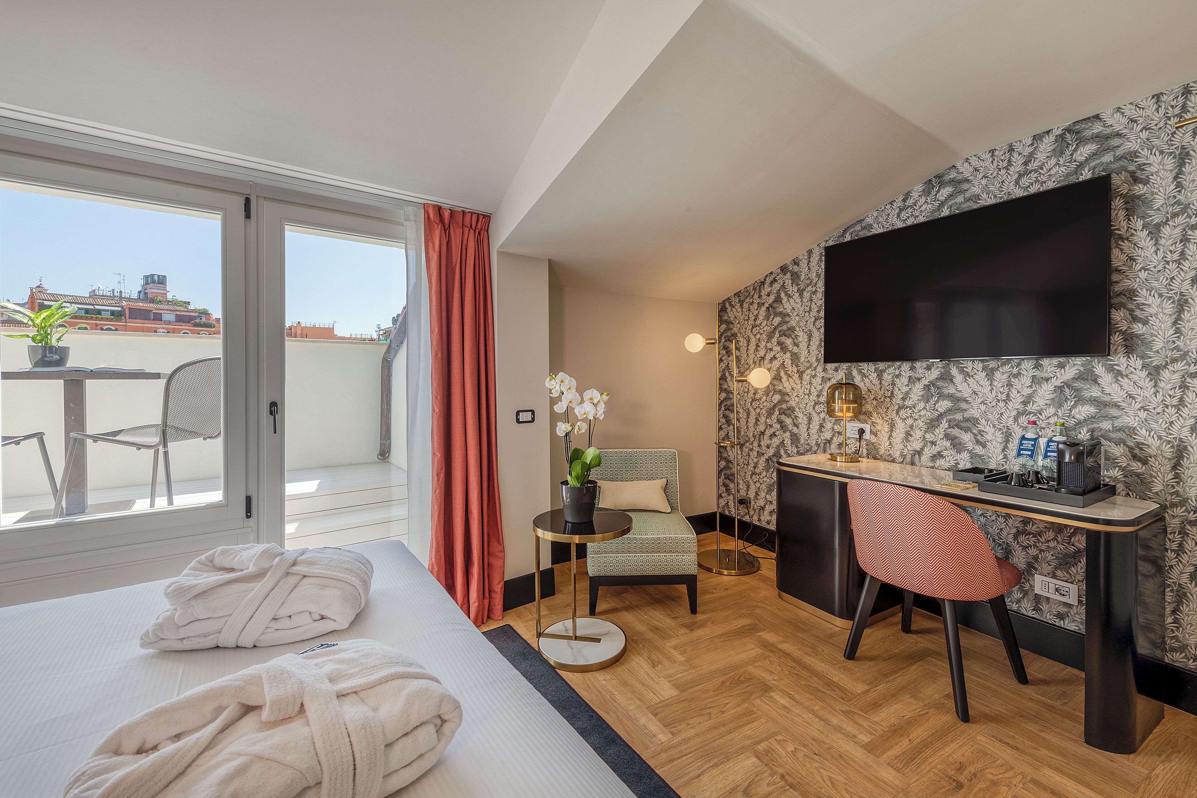 Habitación de hotel con cama, escritorio, silla, televisor y balcón con vista a la ciudad.
