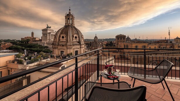 A terrace with a table set for two, overlooking a historic building with domes and towers. - H10 Palazzo Galla (Rome)